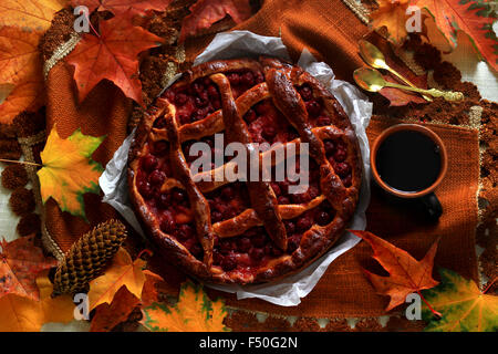 Still Life: Vintage Homemade cherry pie and cup of coffee on dark brown table cloth decorated with autumn leaves Stock Photo