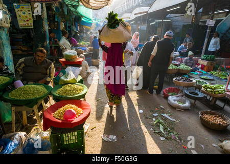 A woman is carrying a bag with vegetables on her head through the vegetable market Stock Photo