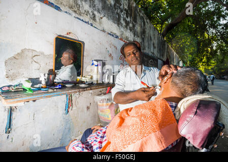 A barber is shaving a customer at his open air shop Stock Photo