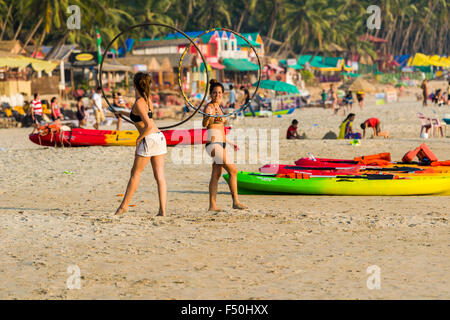 Two young women, wearing bikinis, are playing with a hoop at Palolem Beach with blue sky, palmtrees and white sand Stock Photo