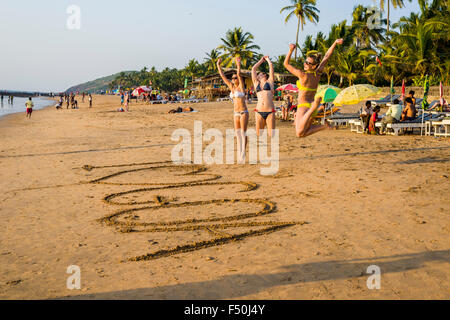 Three young women wearing bikinis are jumping after writing 'I love Goa' in the sand of Anjuna Beach Stock Photo