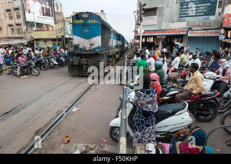 A train is passing a railway crossing, people on motorbikes and pedestrians are waiting behind the closed barriers Stock Photo