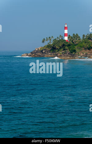 The light house at Kovalam Beach is located on a small peninsula with palmtrees and surrounded by blue water Stock Photo