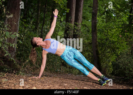 Athletic woman doing a side plank pose on a forest trail Stock Photo