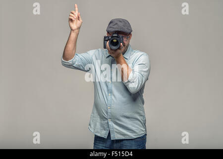 Man in a cap holding his camera to his eye with one hand composing a photograph pointing upwards with his other hand giving inst Stock Photo