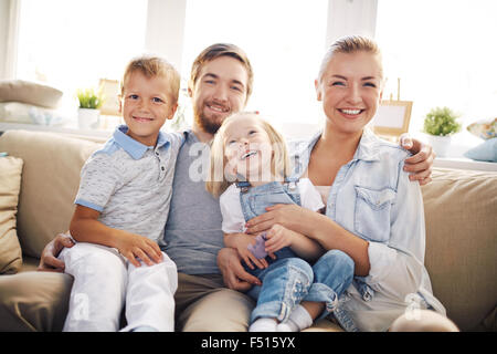 Happy family sitting on sofa at home and looking at camera Stock Photo