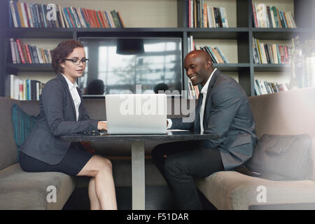 Portrait of two young business colleagues sitting at coffee shop working together on laptop. Diverse business team working at ca Stock Photo