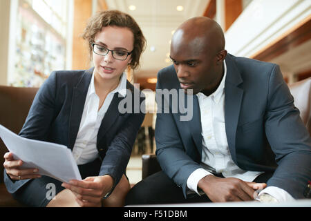 Two business partners sitting together and discussing contract documents. Business executives going through papers in lobby. Stock Photo