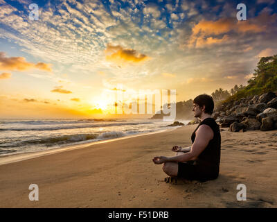 Young fit man do yoga meditation on tropical beach Stock Photo