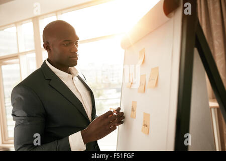 African businessman standing by a whiteboard with sticky notes. Young business executive presenting his ideas on flip board in c Stock Photo