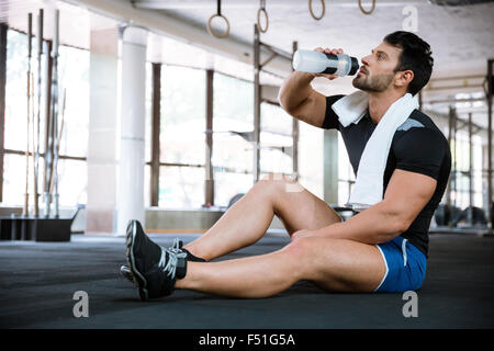 Fitness man wearing blue shorts and black t-shirt sitting on the floor and drinking water Stock Photo