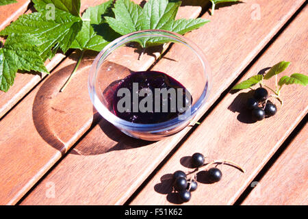 A glass bowl full of tasty black currant jam, in between black currant leaves and berry ripes Stock Photo