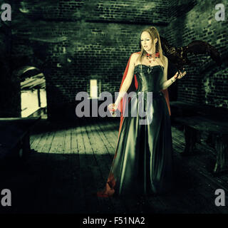 young beautiful female vampire aristocrat with a cup of blood stands in the old castle Stock Photo