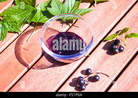 A glass bowl full of tasty black currant jam, in between black currant leaves and berry ripes Stock Photo