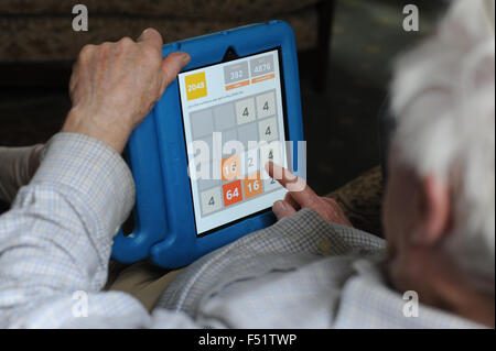 An elderly man playing a game with with a tablet in a living room with his grandchild and sitting on a sofa. Stock Photo