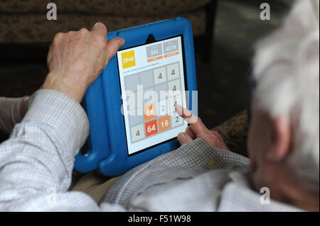 An elderly man playing a game with with a tablet in a living room with his grandchild and sitting on a sofa. Stock Photo