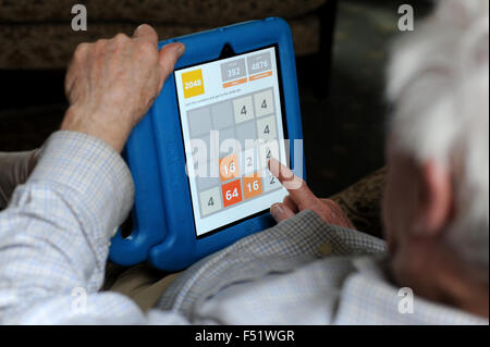 An elderly man playing a game with with a tablet in a living room with his grandchild and sitting on a sofa. Stock Photo