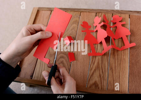Closeup of a woman cutting out a chain of red paper dolls with scissors Stock Photo