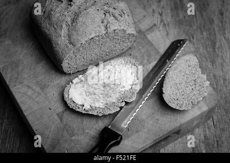 Freshly baked loaf of bread with a buttered slice in black & white Stock Photo