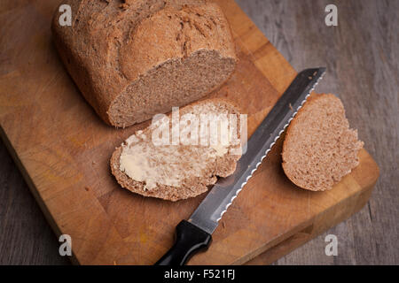 Freshly baked loaf of bread with a buttered slice Stock Photo