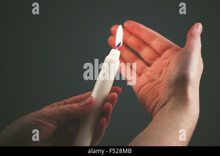 Female hands with burning candle in the dark, woman lighting up the candle as religious ceremony Stock Photo