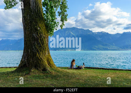 A couple relaxes on Lake Geneva in the summer by a beautiful tree. Lake Geneva, Switzerland. Stock Photo