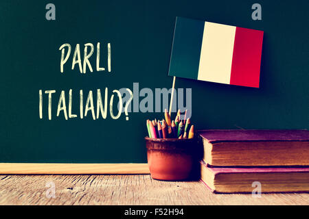 a chalkboard with the question parli italiano? do you speak Italian? written in Italian, a pot with pencils, some books and the Stock Photo