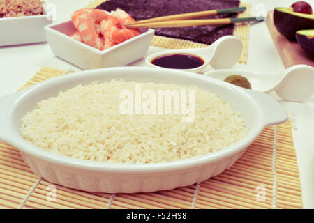 closeup of a table with some of the ingredients and tools to prepare sushi, such as sushi rice, tuna, shrimps, avocado, bamboo m Stock Photo