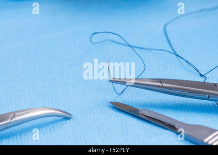 Needle holder with silk suture on blue sterile drape. Stock Photo