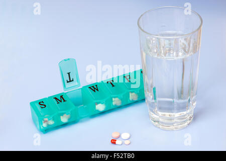 Daily pill dispenser with pills and glass of water. Stock Photo