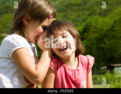 Two twin little sister girls whisper in the ear Stock Photo