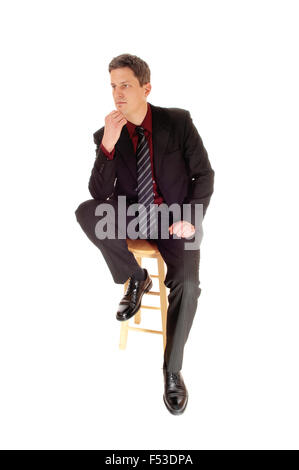 A business man sitting in a suit and tie on a chair with his hand on his chin, thinking hard, isolated for white background. Stock Photo