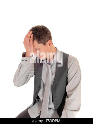 A young man in a grey shirt, tie and vest sitting isolated for white background with one hand on his forehead, thinking. Stock Photo