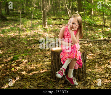 Young girl sitting on a stump in the forest, smiling and looking toward left side of frame, light, and copy space. Stock Photo