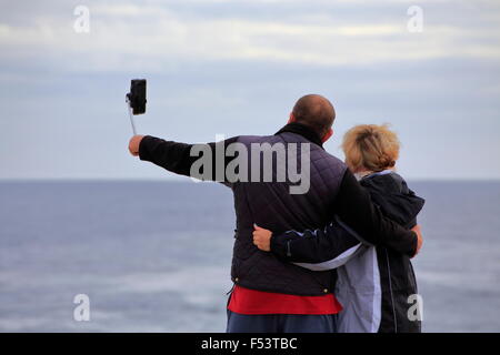 A man and a woman or couple taking a selfie picture with a smartphone on a selfie stick Stock Photo