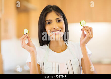 happy Indian girl holding slices of cucumber in kitchen Stock Photo