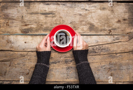 Female hands holding red cup of coffee on wooden background. Top view of morning waking up Stock Photo