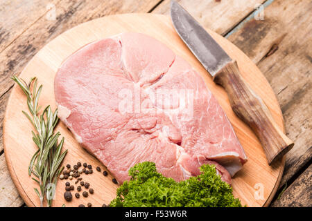 Big chunk of raw beef with rosemary, pepper and knife on cutting board on wooden background. Butcher's background Stock Photo