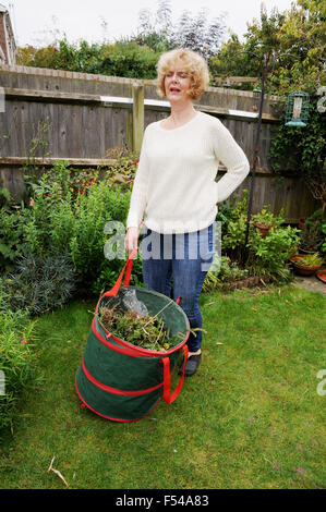 Mature woman gardening lifting heavy bag of garden waste in pain with a bad back ache Stock Photo