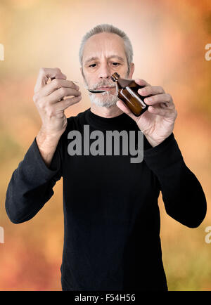 A mature man is pouring cough syrup in a spoon to cure his sore throat and bronchitis Stock Photo