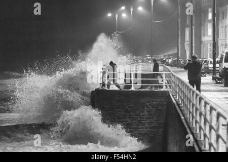 Aberystwyth, Wales, UK. 27th October, 2015. Teenagers take risks as the waves at high tide this evening crash against the promenade in Aberystwyth, while others enjoy the view from a safe distance. Credit:  Ian Jones/Alamy Live News Stock Photo