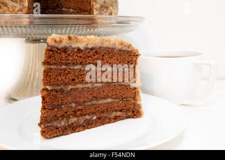 German chocolate cake slice closeup with coffee.  Slice is removed from whole cake which is in background. Stock Photo