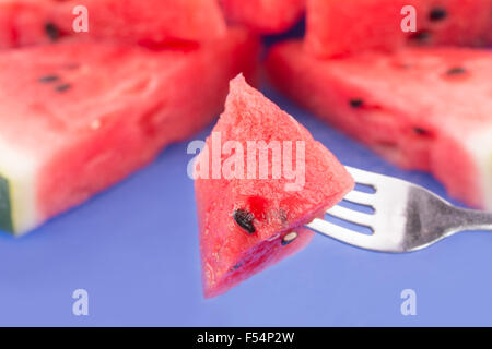 Piece of watermelon on fork, with slices of watermelon on the background on a blue cutting board Stock Photo