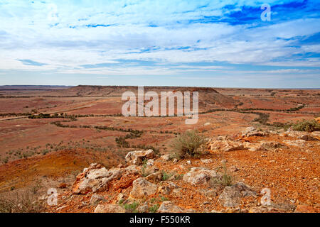Stunning Australian outback landscape from hilltop lookout, rocky mesas on vast barren treeless red plains stretching to horizon & blue sky Stock Photo