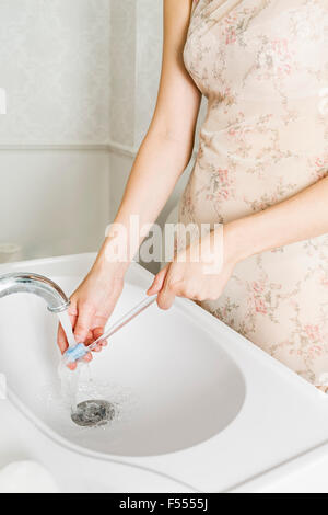 Midsection of woman washing toothbrush at bathroom sink Stock Photo