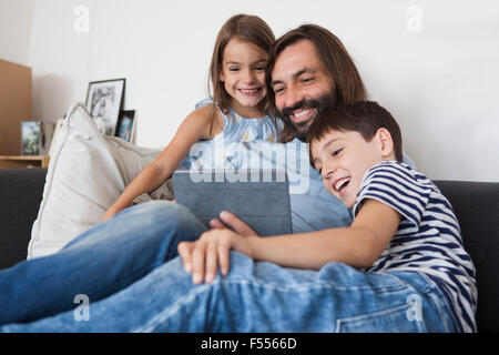 Happy father with children using digital tablet on sofa at home Stock Photo