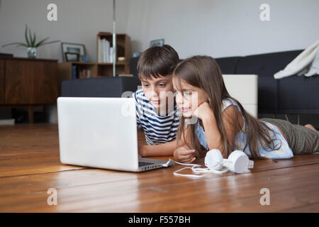 Siblings using laptop while lying on hardwood floor at home Stock Photo