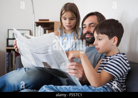 Father and children reading newspaper on sofa at home Stock Photo