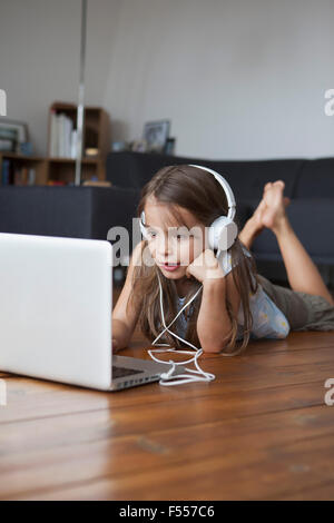 Cute girl listening music while using laptop on hardwood floor at home Stock Photo