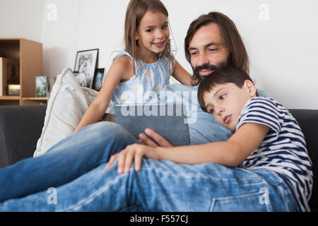 Father with children using digital tablet on sofa at home Stock Photo